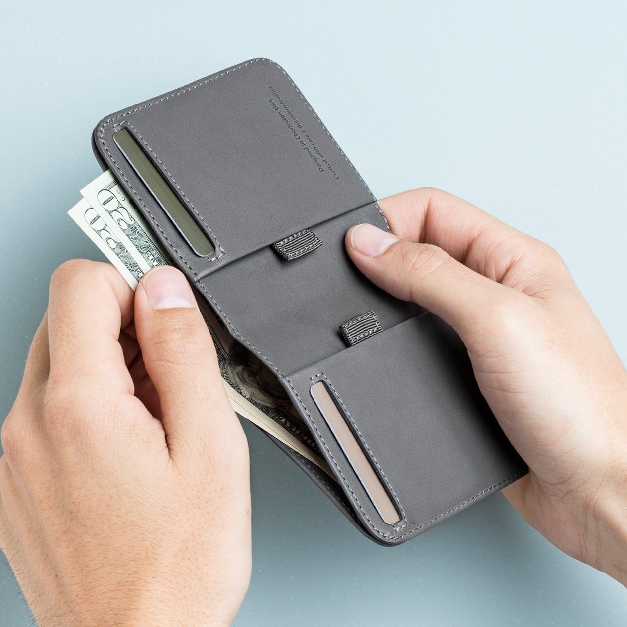two hands taking bills out of a wally agent slim billfold wallet in gray leather designed by distil